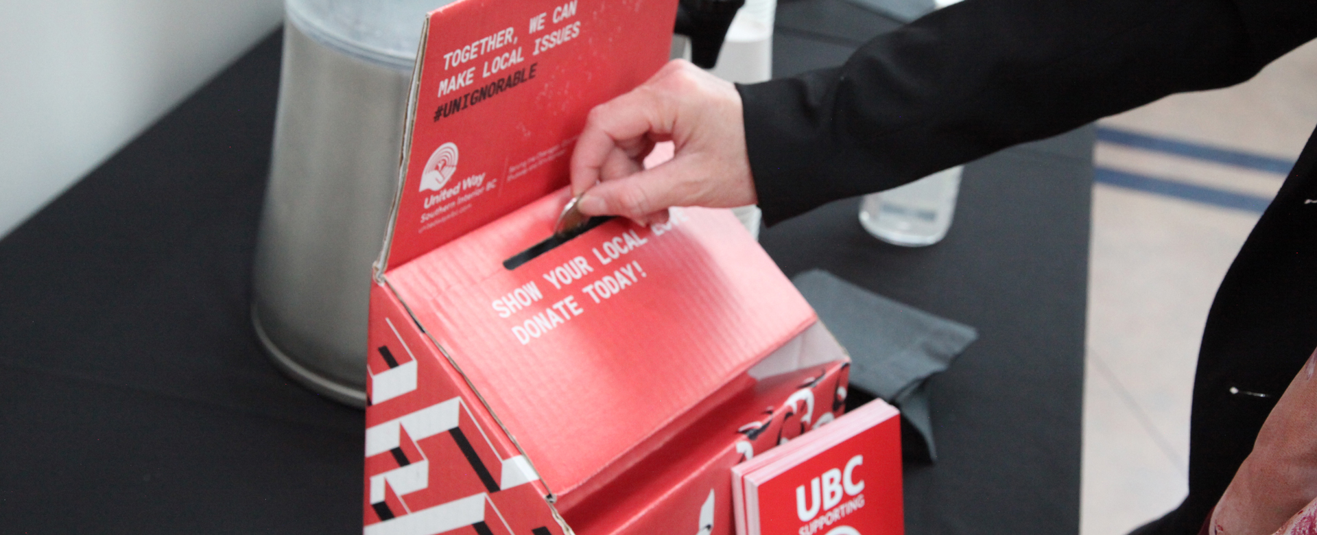 A hand placing a donation in a United Way box